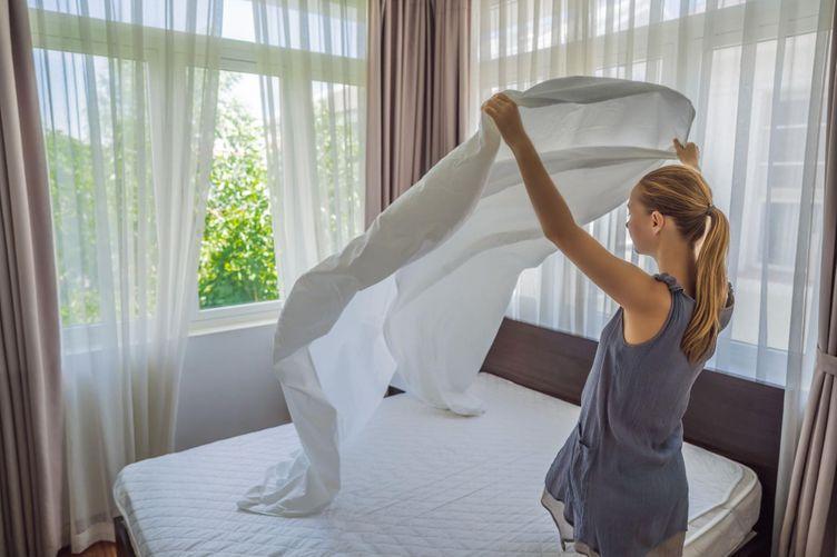 Woman shaking out cotton cooling sheets in airy Timmins bedroom