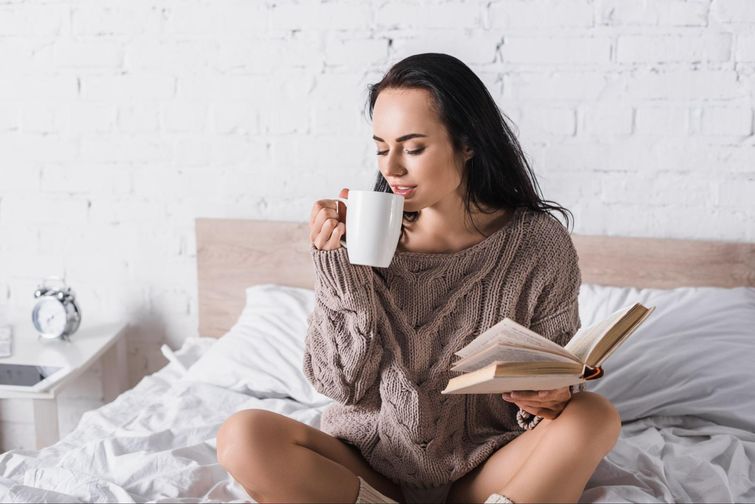 Comfortable woman reading book and drinking coffee on bamboo sheets